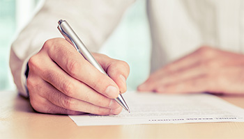 Close-up of a person signing a legal document with a silver pen, representing estate planning